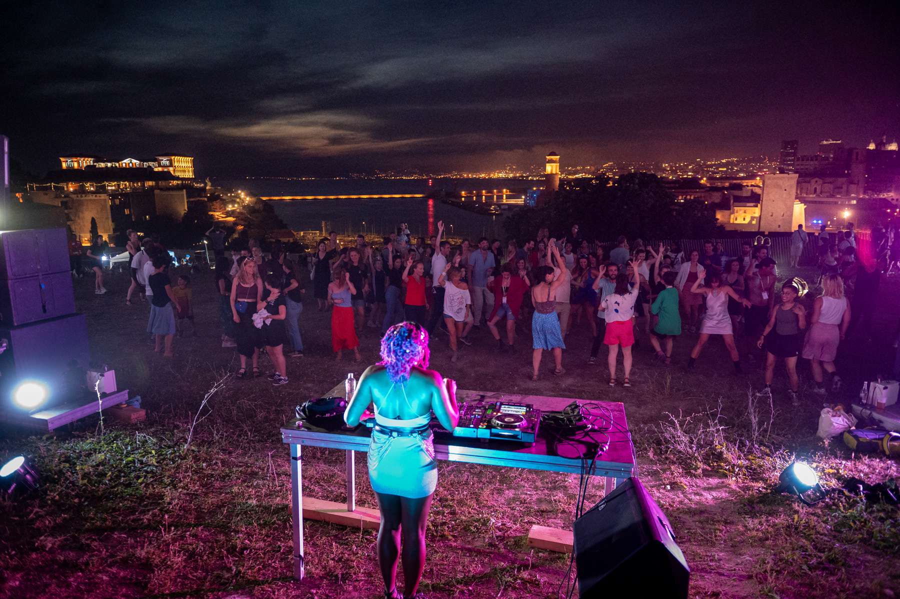 DJ de dos devant une foule qui danse dans une lumière violette en extérieur