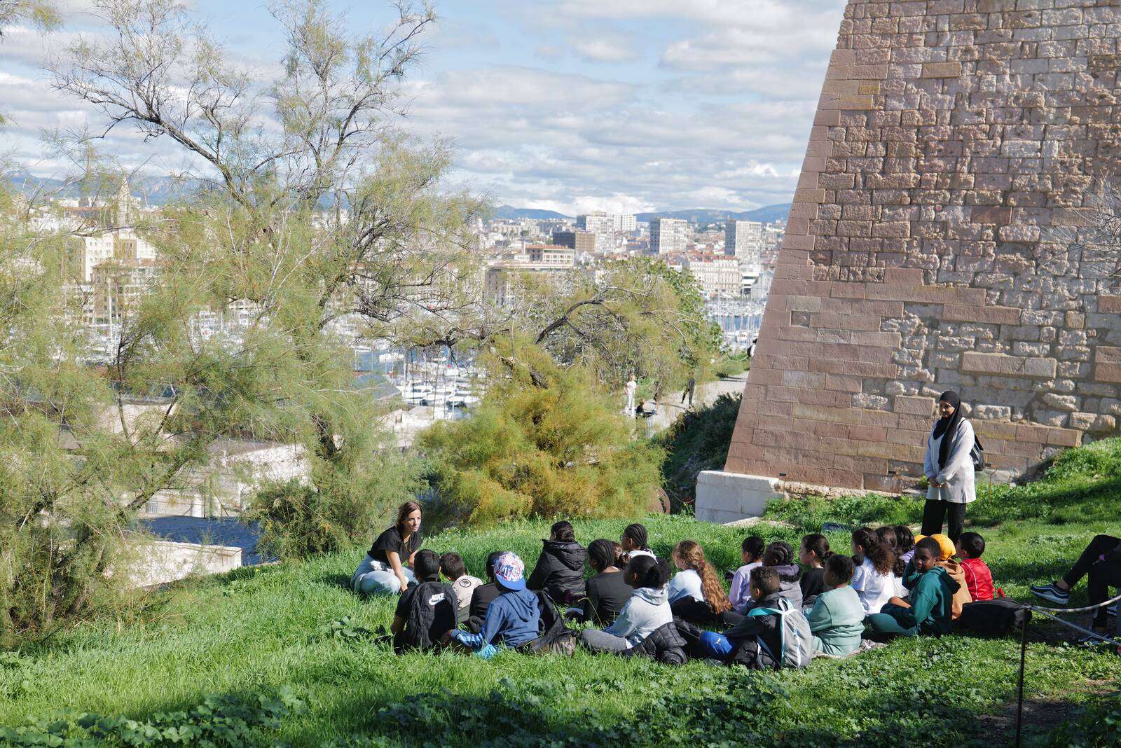 Enfants assis dans l'herbe face à une adulte